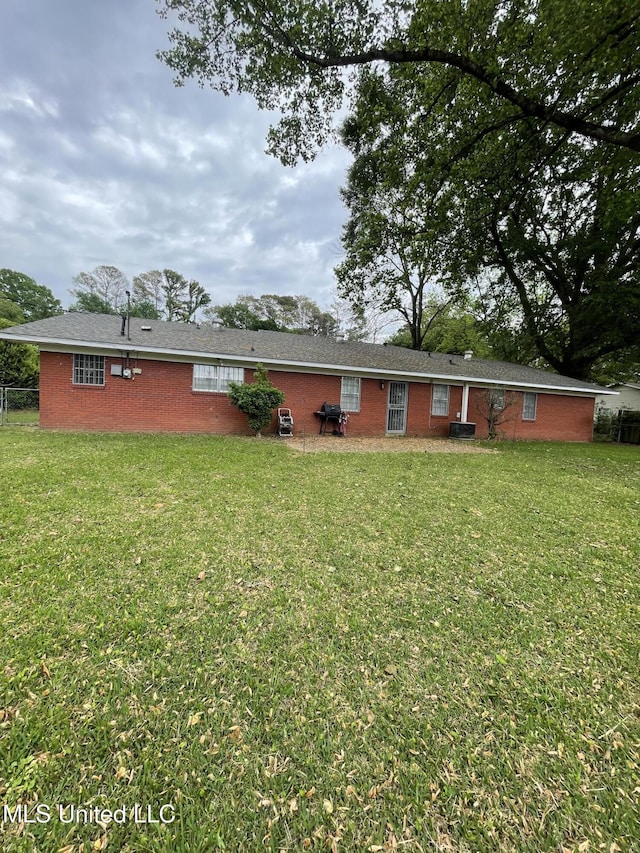 rear view of property with a lawn, fence, and brick siding