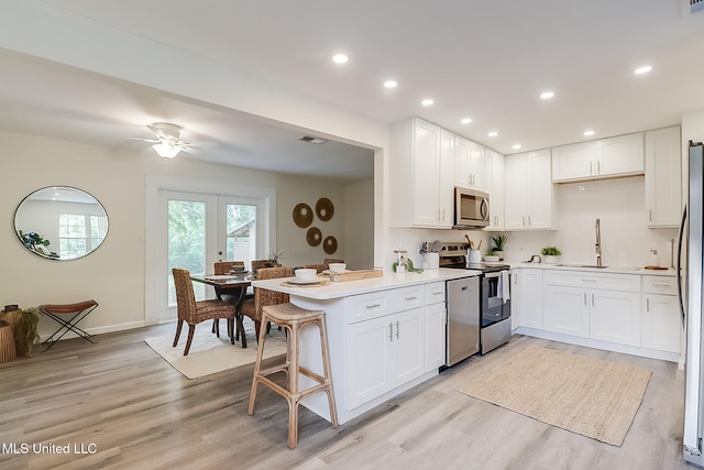 kitchen with light wood finished floors, a peninsula, white cabinets, a sink, and appliances with stainless steel finishes