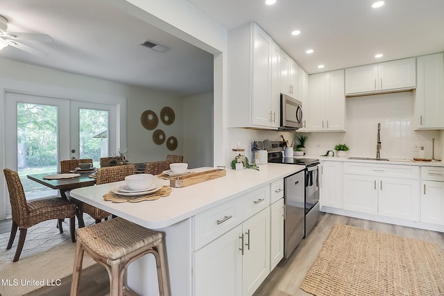 kitchen featuring stainless steel appliances, a sink, visible vents, light wood-style floors, and white cabinetry