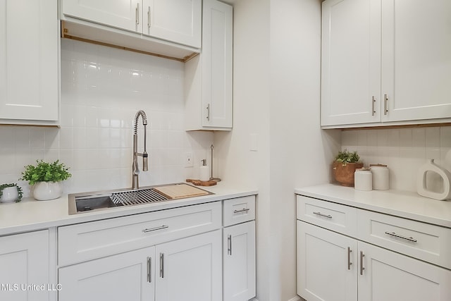 kitchen featuring white cabinets, decorative backsplash, light countertops, and a sink