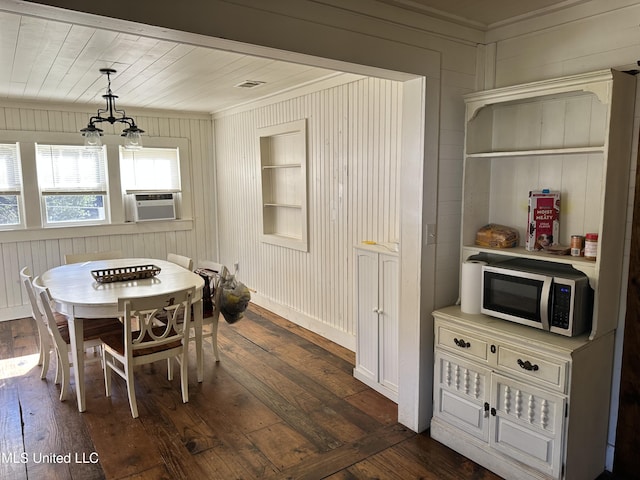 dining room featuring wooden walls, dark wood-type flooring, built in shelves, and a notable chandelier