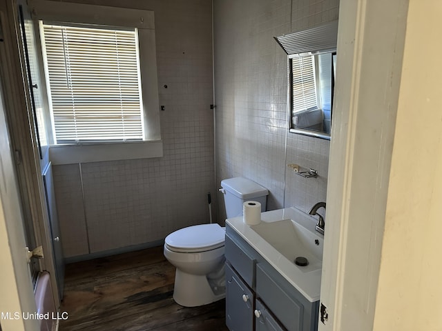 half bathroom featuring tile walls, toilet, a healthy amount of sunlight, vanity, and wood finished floors