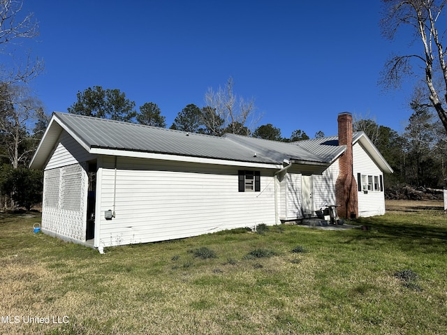 exterior space featuring a chimney, metal roof, and a lawn