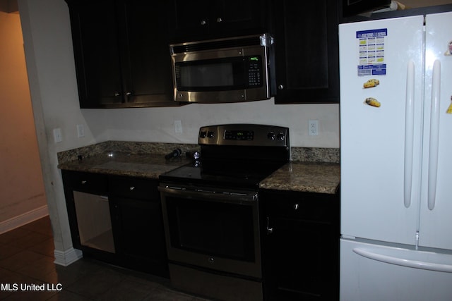 kitchen featuring stainless steel appliances, dark tile patterned flooring, and dark stone counters