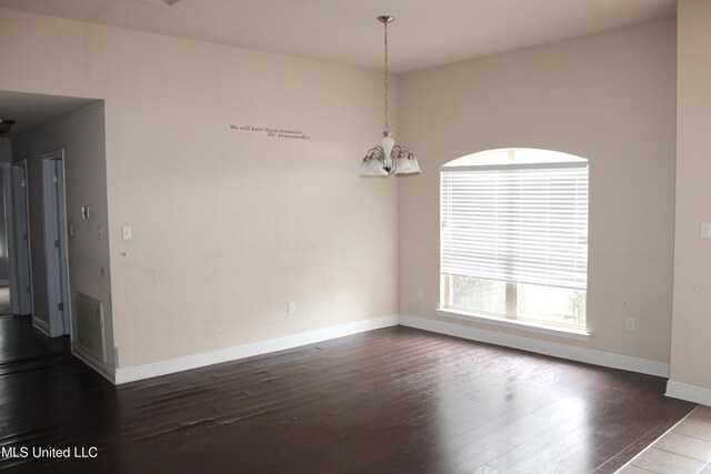 empty room with wood-type flooring and a chandelier