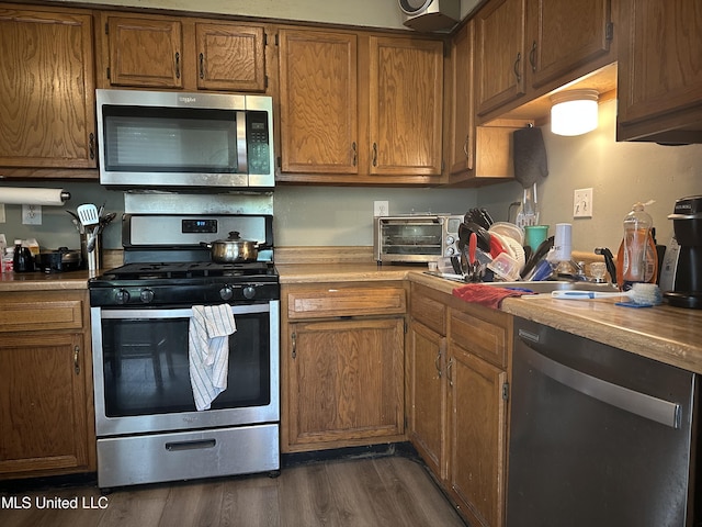 kitchen featuring a toaster, a sink, dark wood-type flooring, brown cabinets, and appliances with stainless steel finishes