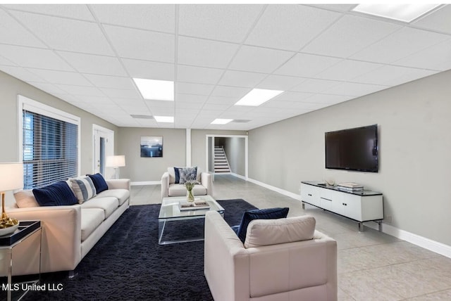 living room featuring stairs, baseboards, a drop ceiling, and light tile patterned flooring