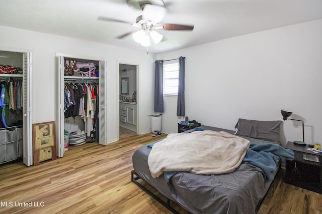 bedroom with light wood-style flooring, a ceiling fan, ensuite bath, and multiple closets