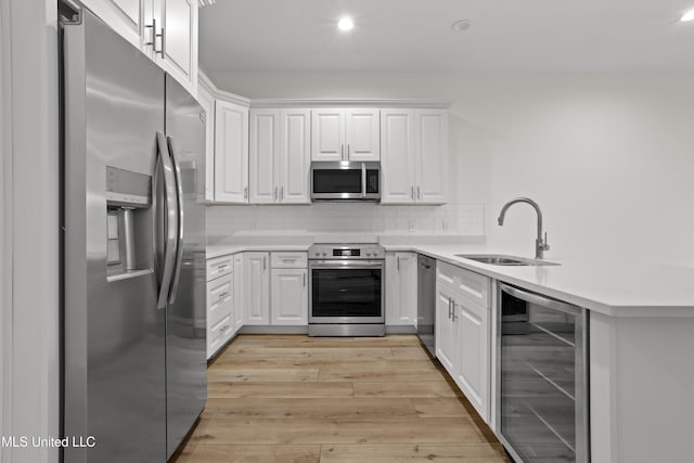 124 Court St, Bay Saint Louis, MS 39520 - kitchen featuring appliances with stainless steel finishes, wine cooler, light wood finished floors, a peninsula, and white cabinets