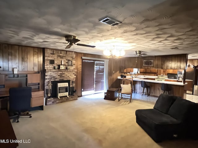 living room with light carpet, wooden walls, ceiling fan with notable chandelier, and a brick fireplace