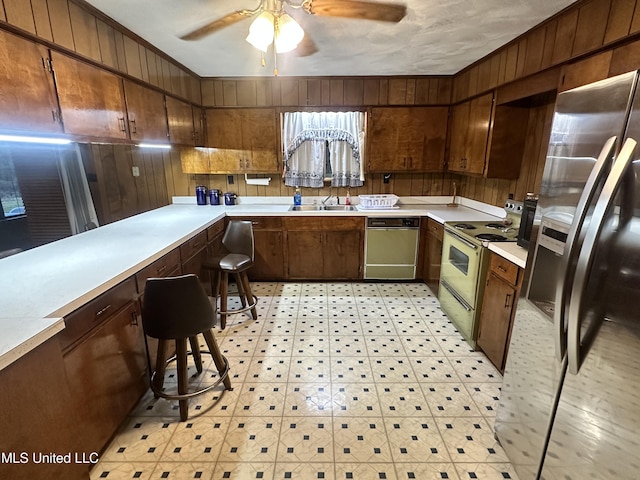 kitchen featuring ceiling fan, sink, stainless steel refrigerator with ice dispenser, white range with electric stovetop, and wood walls