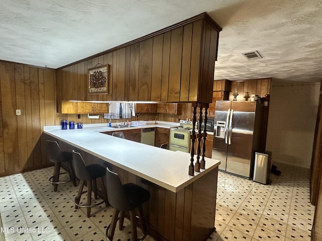 kitchen with kitchen peninsula, a breakfast bar, stainless steel appliances, wooden walls, and sink