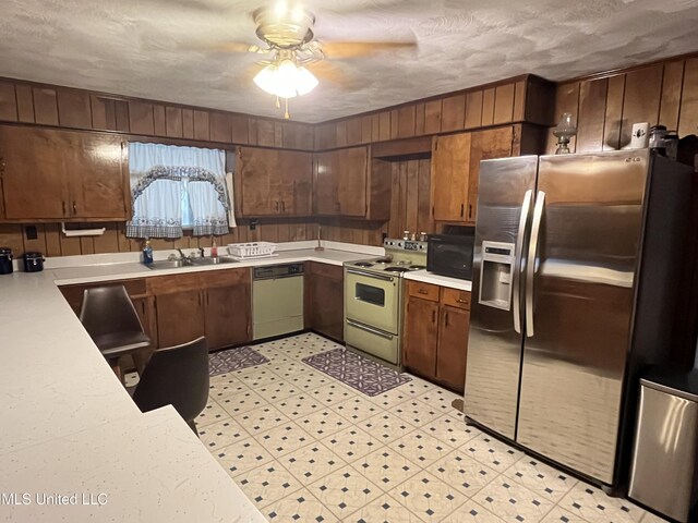 kitchen featuring a textured ceiling, white appliances, ceiling fan, sink, and wood walls