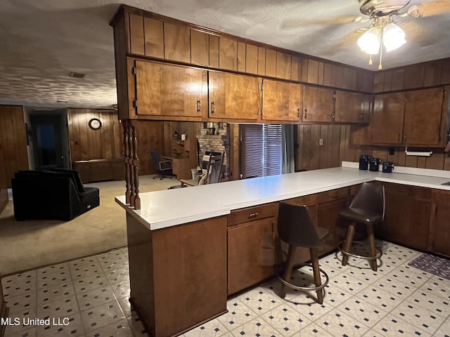 kitchen featuring ceiling fan, kitchen peninsula, wood walls, a textured ceiling, and light carpet