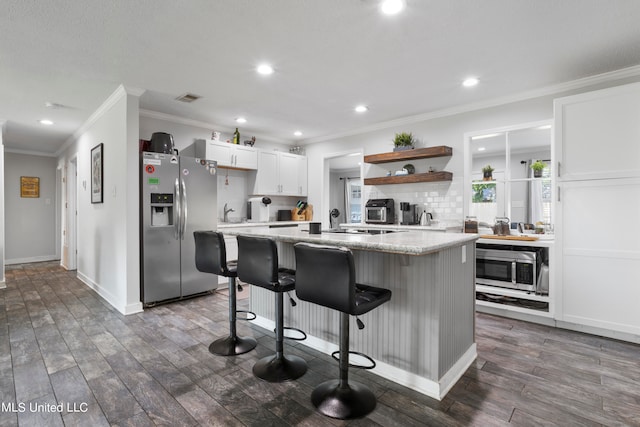 kitchen with appliances with stainless steel finishes, a kitchen bar, white cabinetry, dark wood-type flooring, and light stone counters