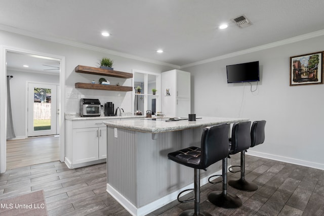 kitchen with a breakfast bar, white cabinets, crown molding, and dark hardwood / wood-style flooring