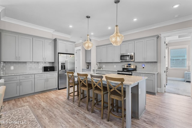 kitchen featuring light wood-style flooring, ornamental molding, gray cabinets, stainless steel appliances, and a kitchen bar