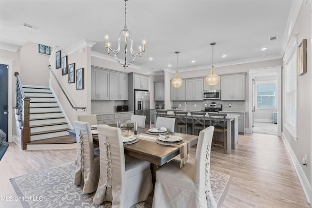 dining area featuring ornamental molding, light wood-type flooring, visible vents, and stairs