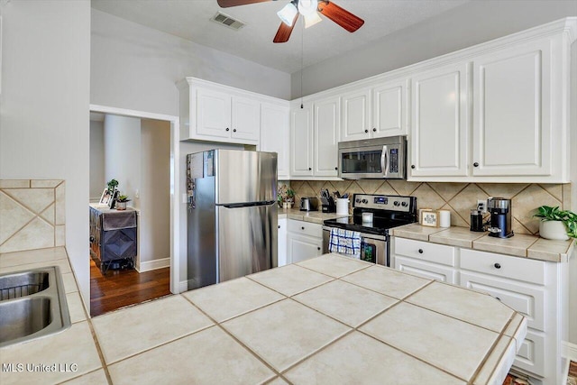 kitchen with ceiling fan, appliances with stainless steel finishes, tasteful backsplash, a sink, and tile counters