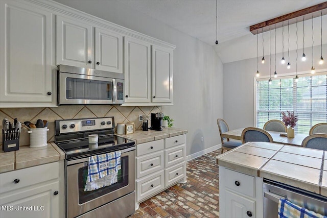 kitchen featuring appliances with stainless steel finishes, brick floor, tile counters, baseboards, and tasteful backsplash