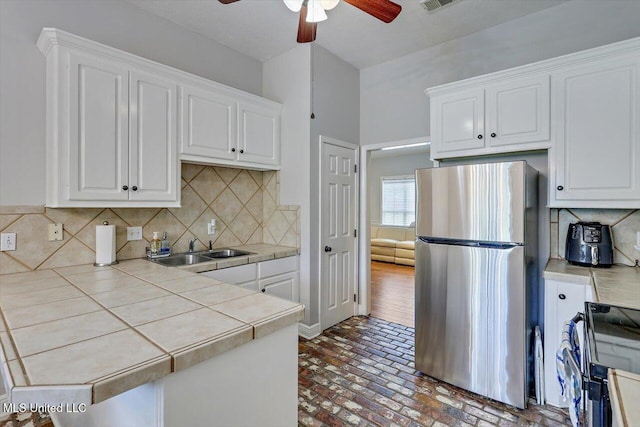 kitchen featuring a ceiling fan, electric range, tile counters, freestanding refrigerator, and brick floor