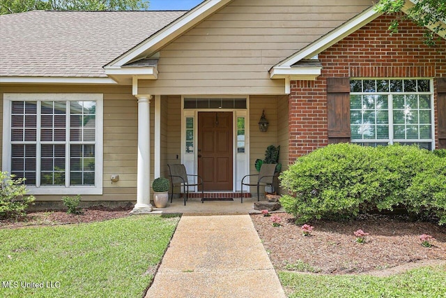 entrance to property featuring a shingled roof, a porch, and brick siding