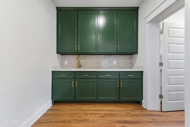 bar featuring sink, light wood-type flooring, decorative backsplash, and green cabinets