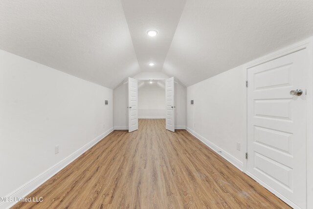 additional living space featuring vaulted ceiling, light hardwood / wood-style floors, and a textured ceiling