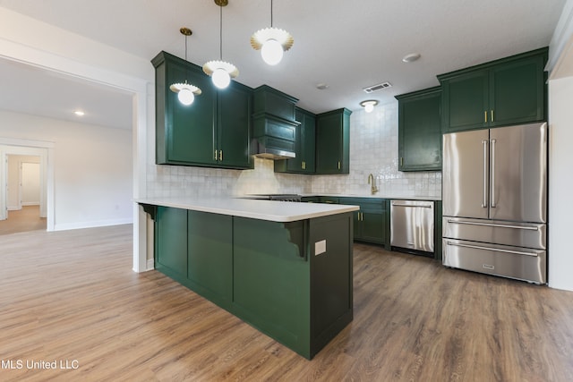 kitchen with appliances with stainless steel finishes, hanging light fixtures, hardwood / wood-style flooring, a breakfast bar, and kitchen peninsula