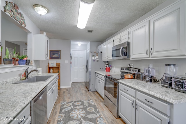 kitchen with stainless steel appliances, light countertops, visible vents, white cabinets, and a sink