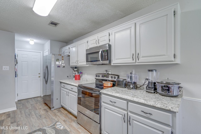 kitchen with stainless steel appliances, light countertops, visible vents, light wood-style flooring, and white cabinets