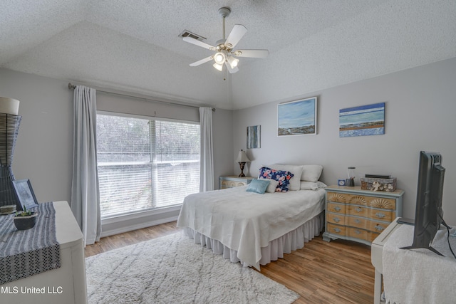 bedroom with light wood-type flooring, visible vents, a textured ceiling, and lofted ceiling