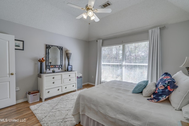 bedroom with lofted ceiling, a textured ceiling, visible vents, baseboards, and light wood-style floors