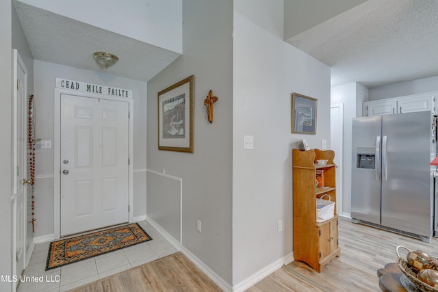 foyer entrance with light wood finished floors, baseboards, and a textured ceiling