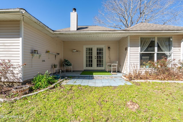 rear view of house with french doors, a lawn, a chimney, and a patio