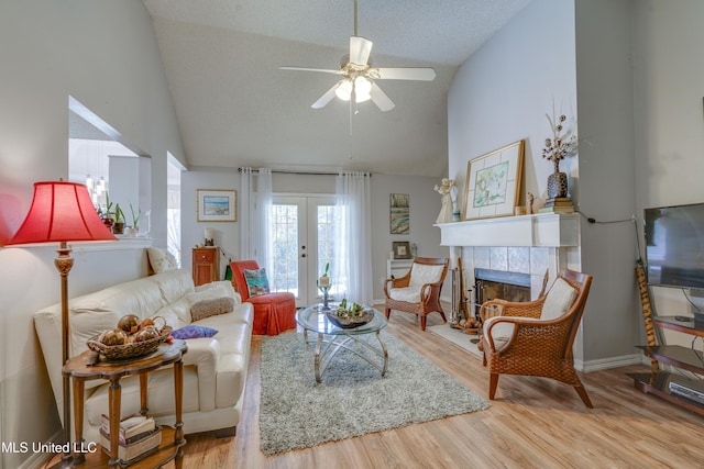 living room featuring french doors, light wood-style flooring, a ceiling fan, a textured ceiling, and a tile fireplace