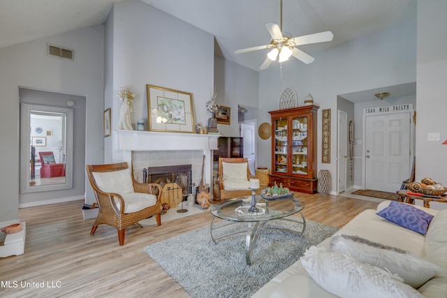 living area with high vaulted ceiling, light wood finished floors, a tiled fireplace, and visible vents