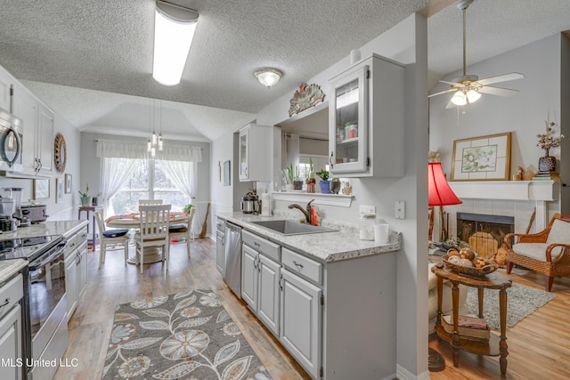 kitchen featuring a tile fireplace, stainless steel appliances, a sink, light wood-type flooring, and glass insert cabinets