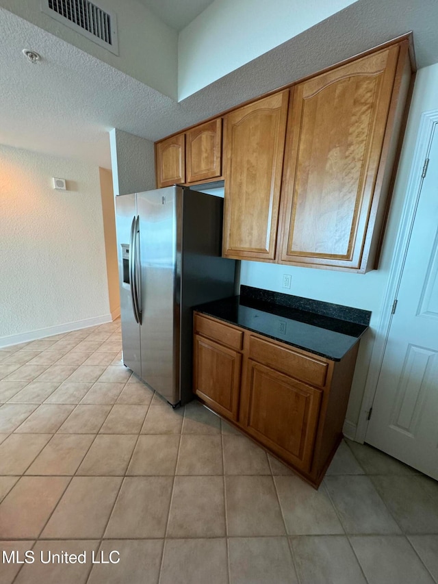 kitchen with a textured ceiling, light tile patterned floors, and stainless steel refrigerator with ice dispenser