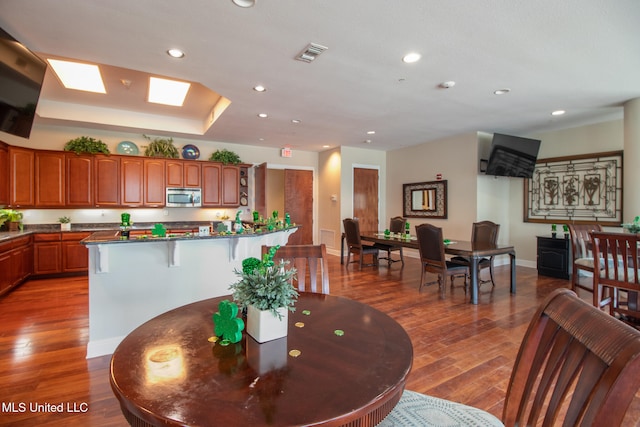 kitchen featuring a raised ceiling, wood-type flooring, a center island, and a kitchen breakfast bar