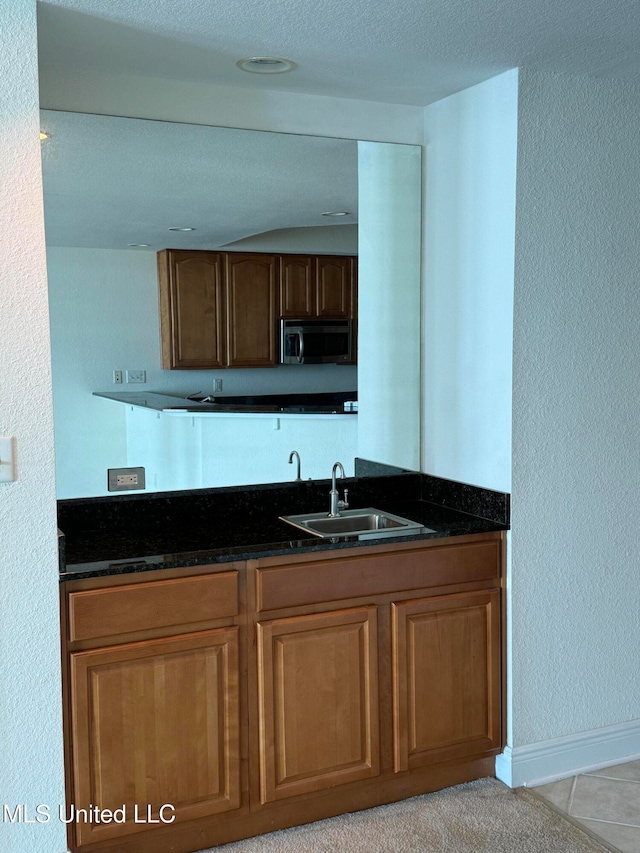 kitchen featuring light tile patterned flooring, dark stone countertops, sink, and a textured ceiling