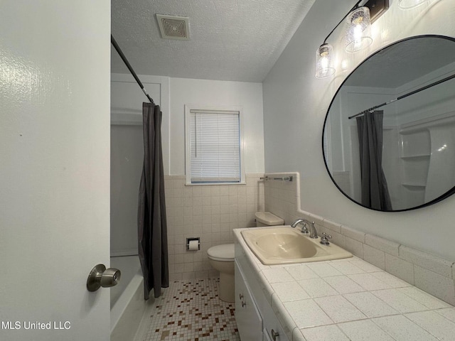 full bath featuring visible vents, tile walls, toilet, wainscoting, and a textured ceiling