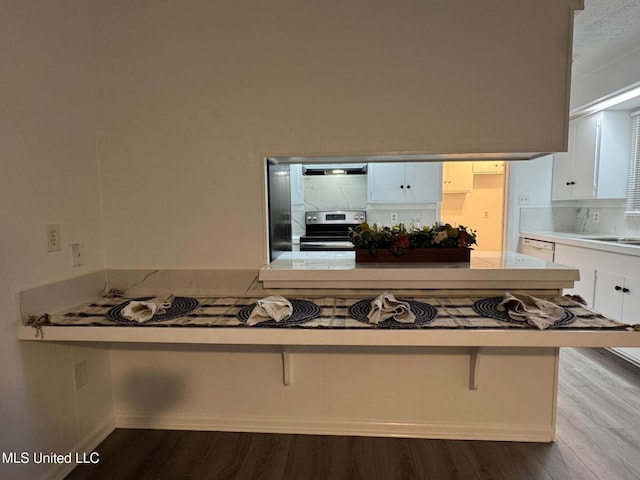 kitchen with backsplash, stainless steel electric stove, light countertops, wood finished floors, and white cabinets