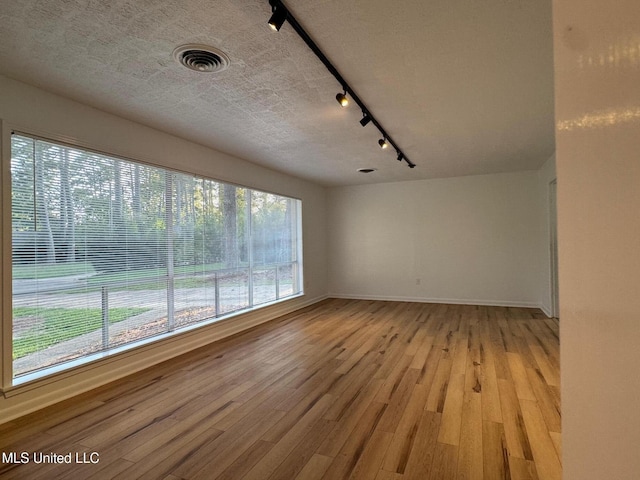 unfurnished room with baseboards, visible vents, light wood finished floors, track lighting, and a textured ceiling