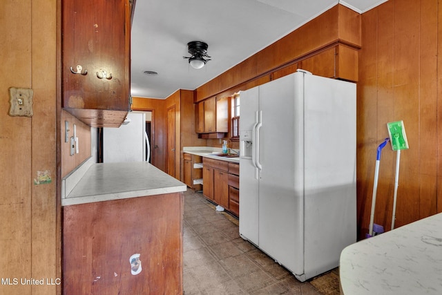 kitchen featuring sink, white refrigerator with ice dispenser, wooden walls, and white refrigerator