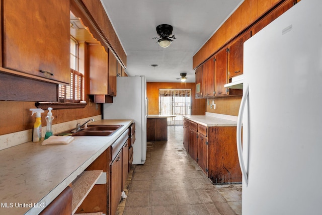 kitchen featuring ceiling fan, sink, white fridge, and wood walls