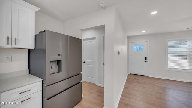 kitchen with light wood finished floors, stainless steel fridge with ice dispenser, light countertops, white cabinetry, and baseboards