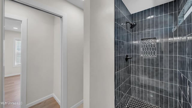 full bath featuring baseboards, a tile shower, and wood finished floors