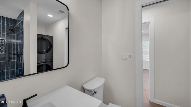 bathroom with stacked washer and dryer, visible vents, tiled shower, toilet, and wood finished floors