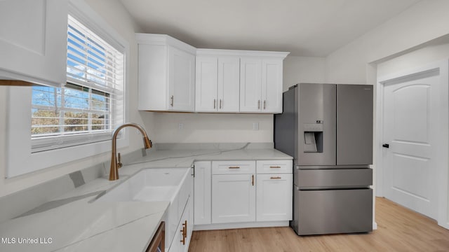 kitchen featuring light stone counters, white cabinets, a sink, light wood-type flooring, and stainless steel fridge